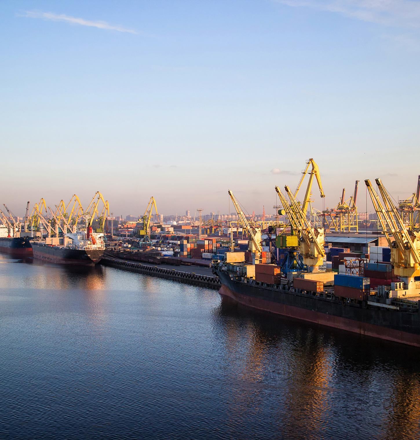 Commercial vessels and cargo cranes at a Saudi port during golden hour